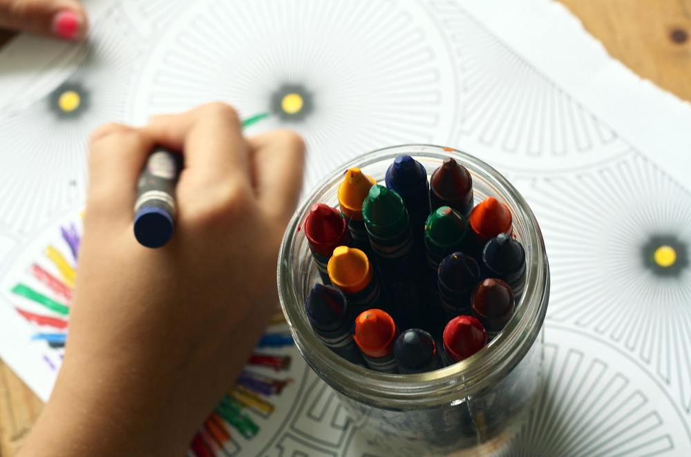 A childs hand holding a crayon next to a jar filled with crayons