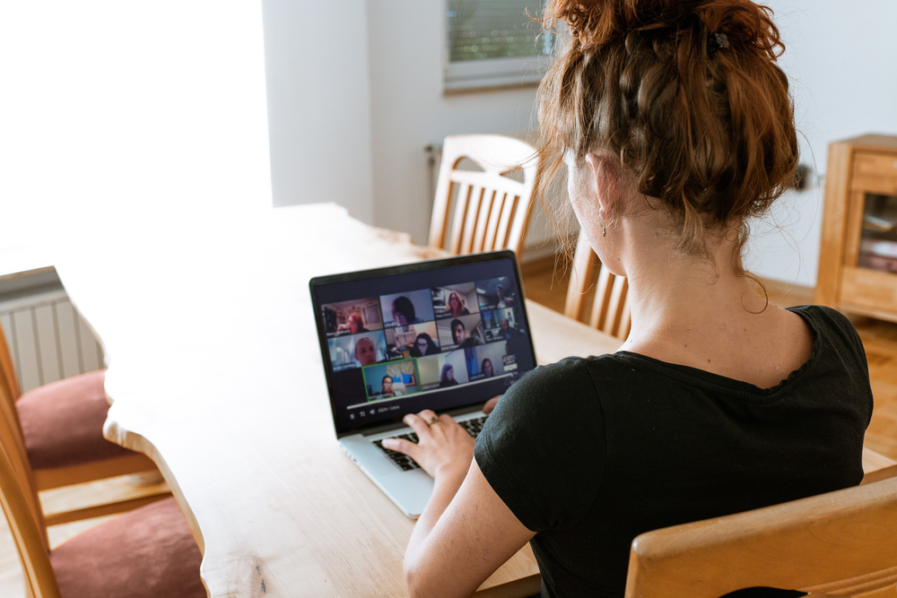 The back of a womans head as she looks down at a virtual meeting on her laptop