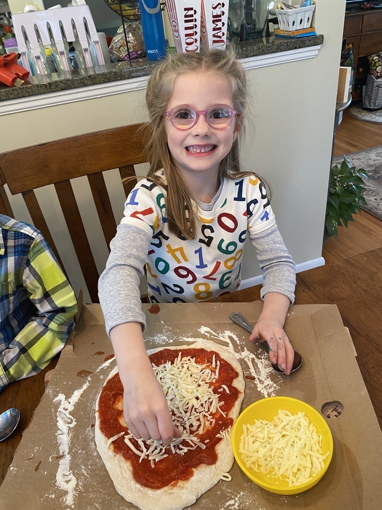 picture of a student creating her homemade pizza . adding the cheese to the pie